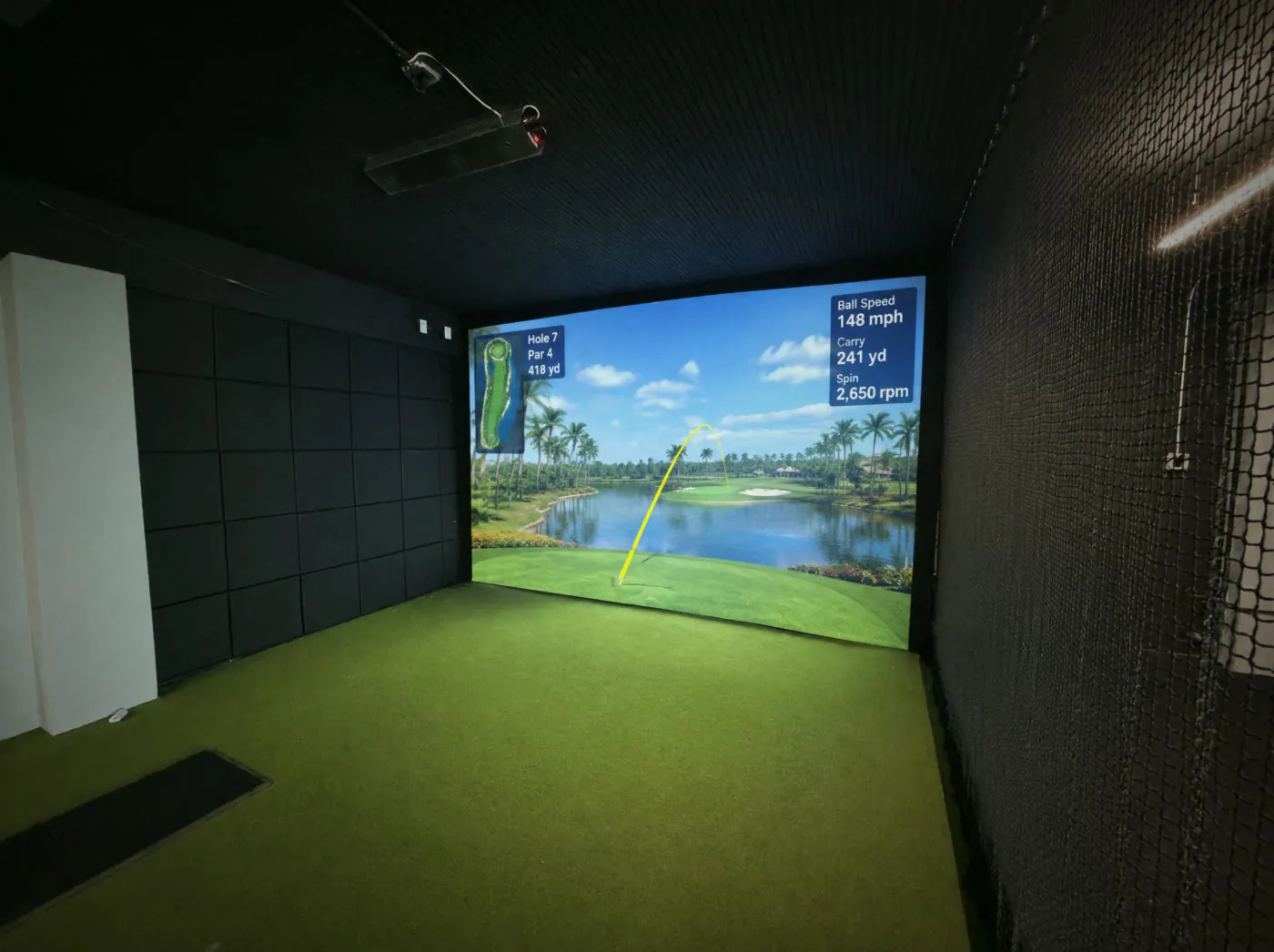 Golf simulator room with acoustic wall panels, safety netting and an overhead launch monitor