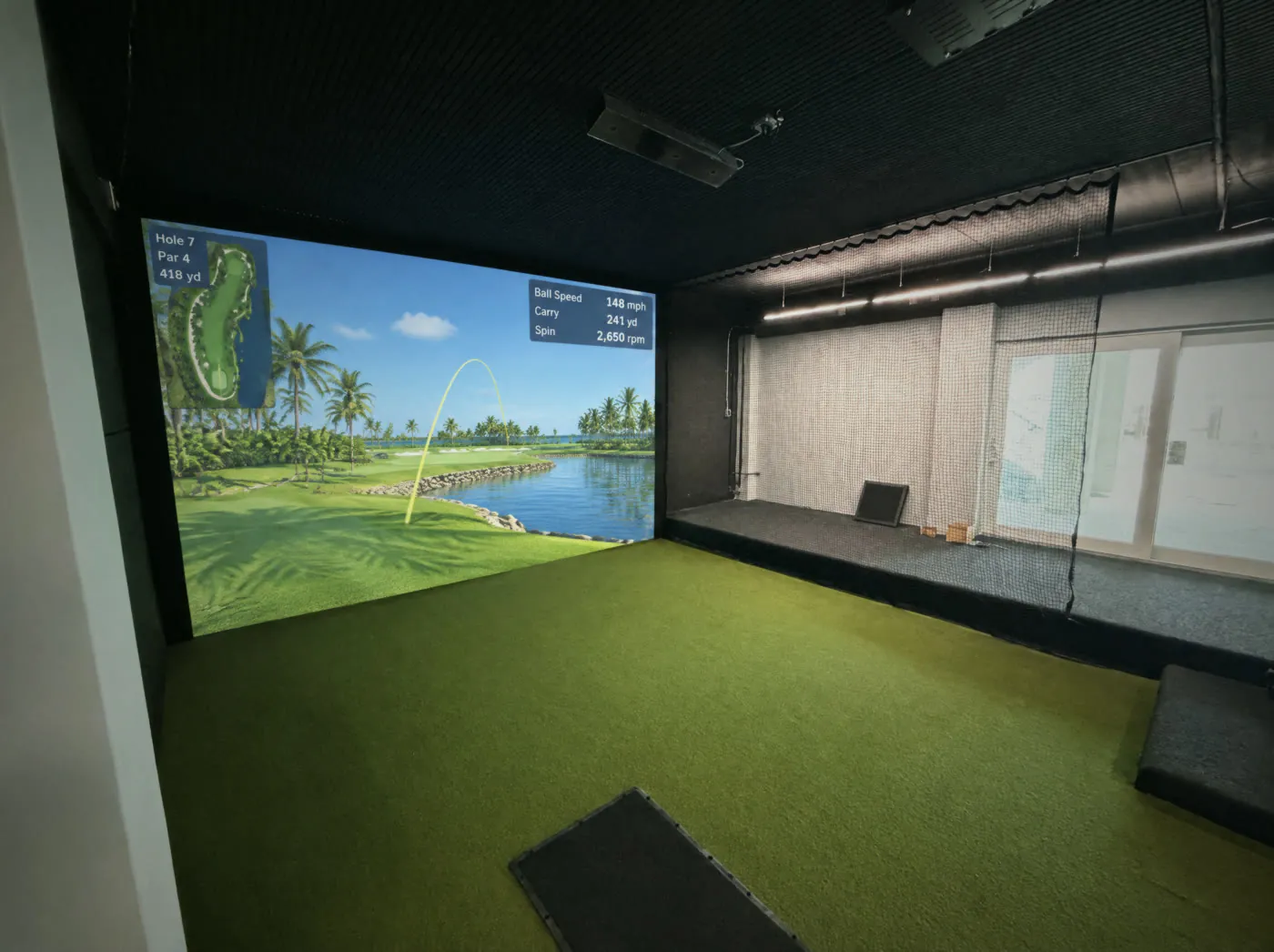 Golf simulator room with the impact screen on, safety netting and sliding doors to the water