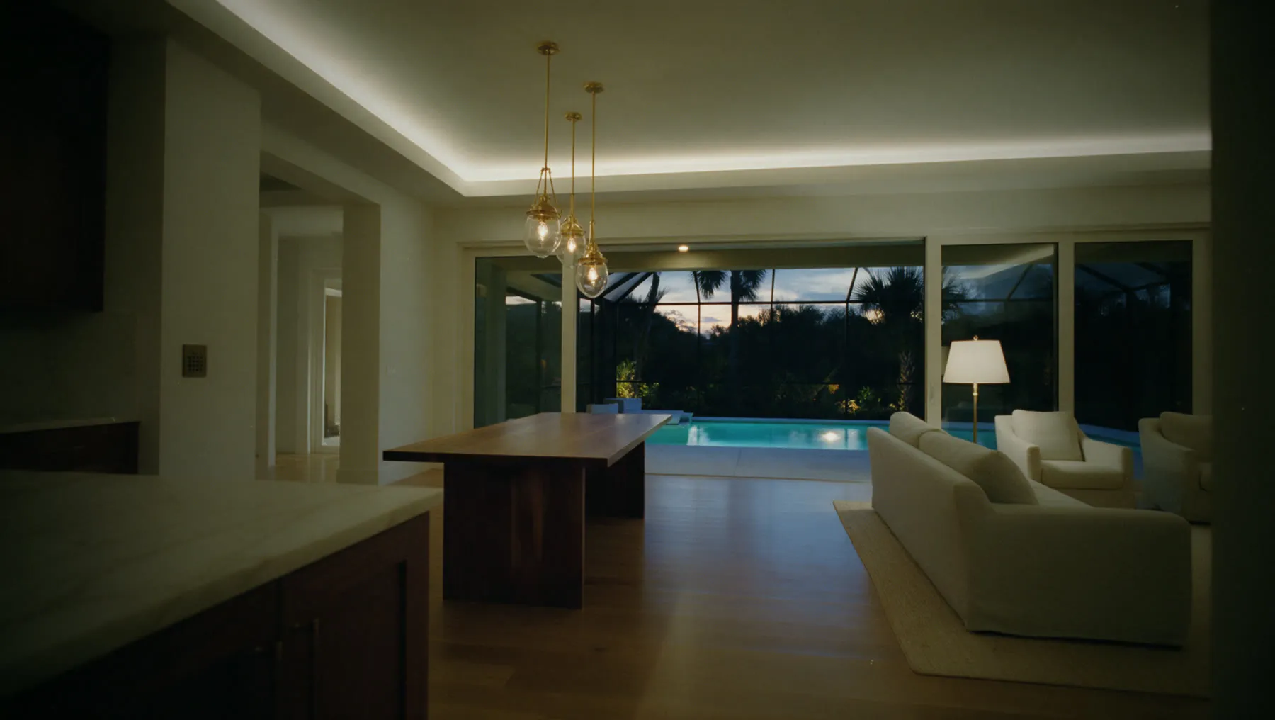Gulf Coast great room, Sera scene at 19:30: Every shade lifts for the sunset. Pendants and cove come up to 30%, the lamp by the sofa, the lanai and the pool.