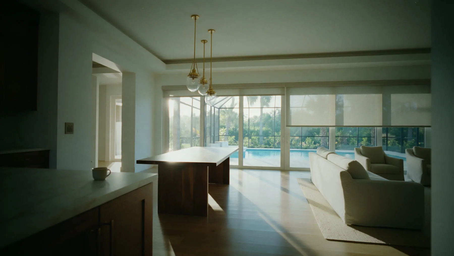 Gulf Coast great room, Alba scene at 07:00: East shades rise, the west side stays down to hold the cool. Lights stay off; the coffee station wakes.